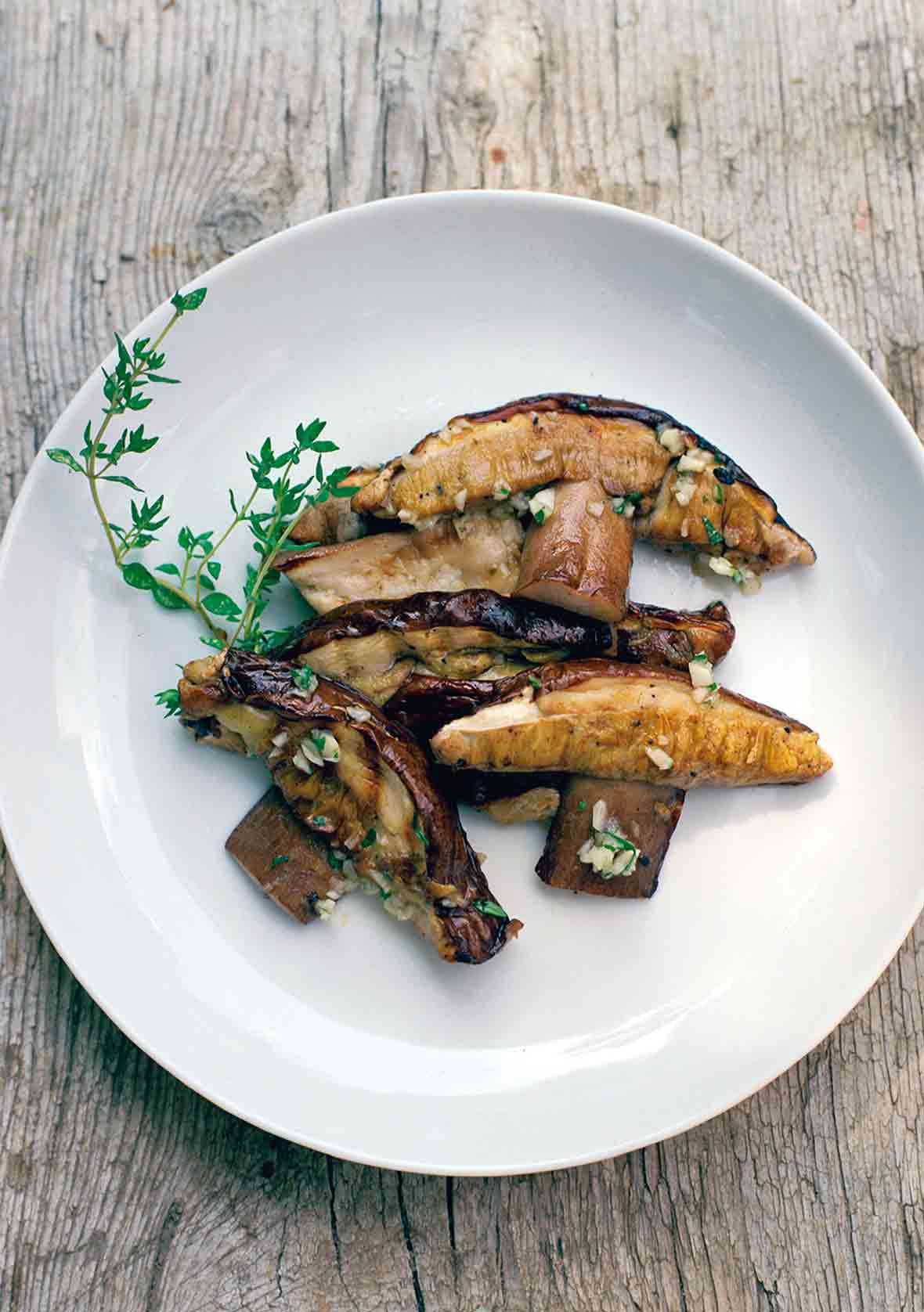 A white plate filled with sliced grilled porcini mushrooms with mint and garlic, garnished with a sprig of thyme.