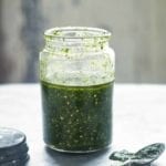Glass jar of pumpkin seed pesto, nearby the lid and a spoon with pesto