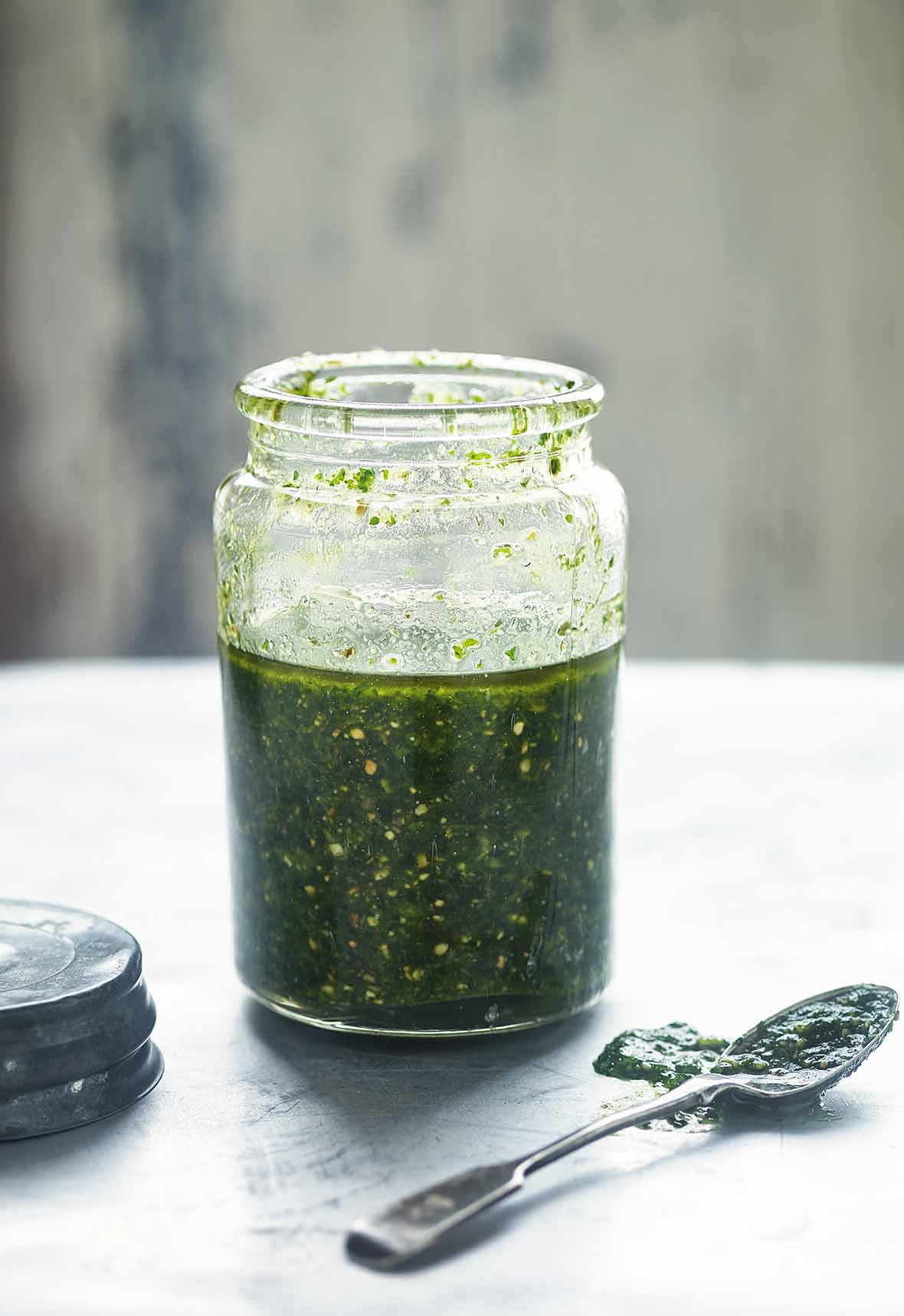 Glass jar of pumpkin seed pesto, nearby the lid and a spoon with pesto
