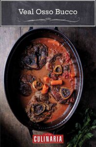 Five veal osso bucco, with carrots, and tomato sauce in. a black cast-iron pot.