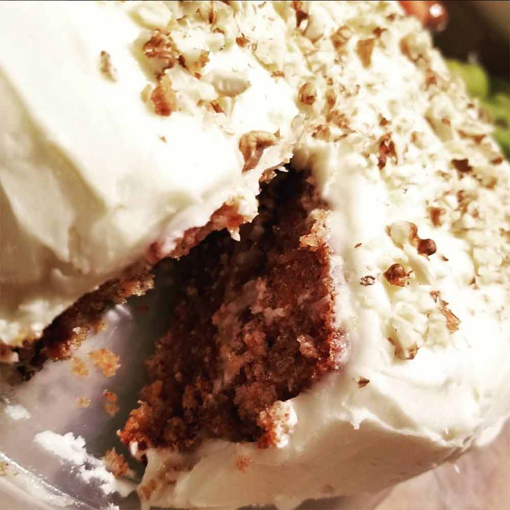 A carrot cake, with a slice removed, covered in cream cheese frosting and sprinkled with walnuts