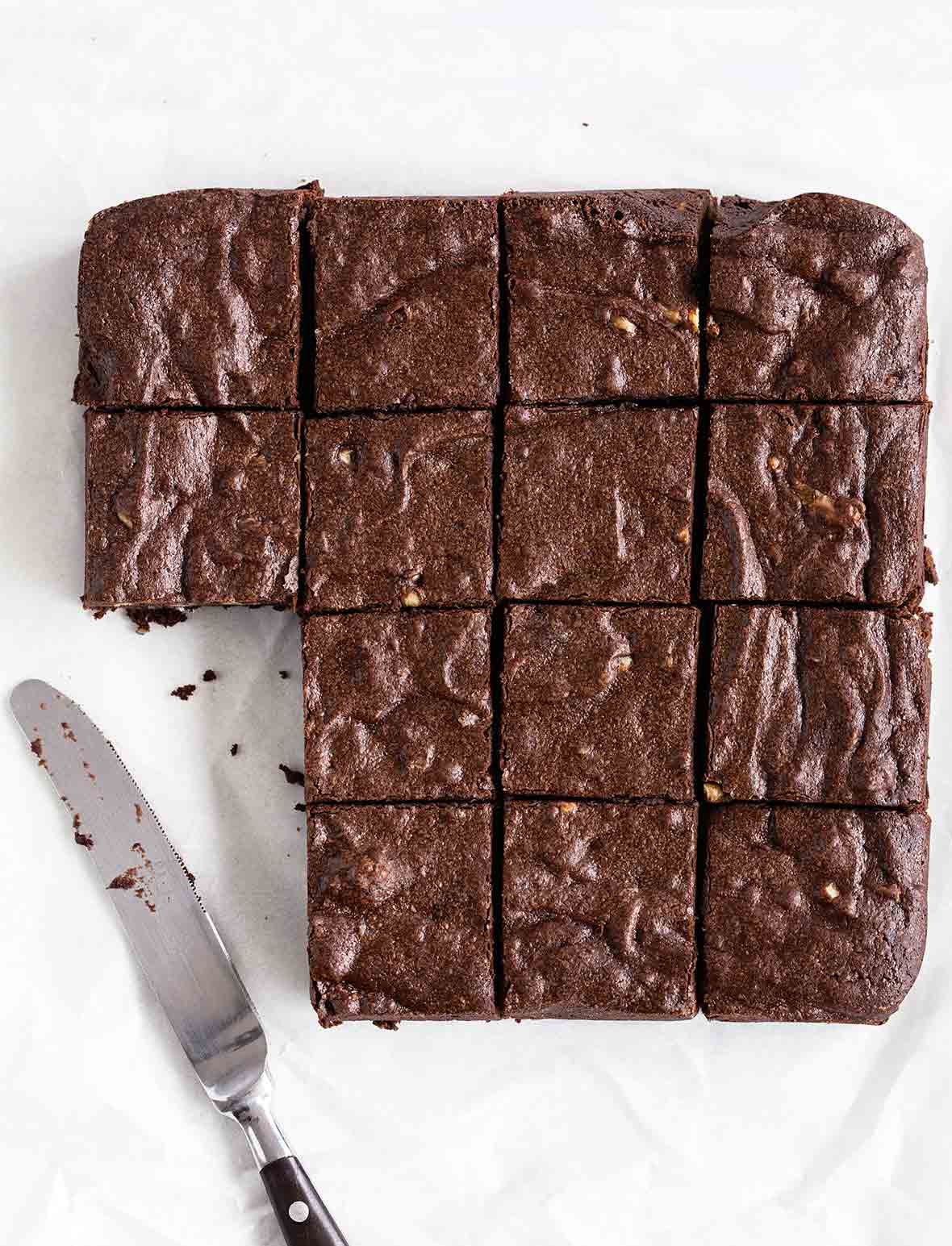 14 fat, chocolatey fudgy pudgy brownies sliced, with a table knife nearby with crumbs