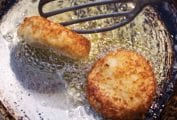 Old frying pan with two leftover mashed potato cakes being turned by a spatula.