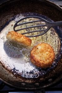 Old frying pan with two leftover mashed potato cakes being turned by a spatula.