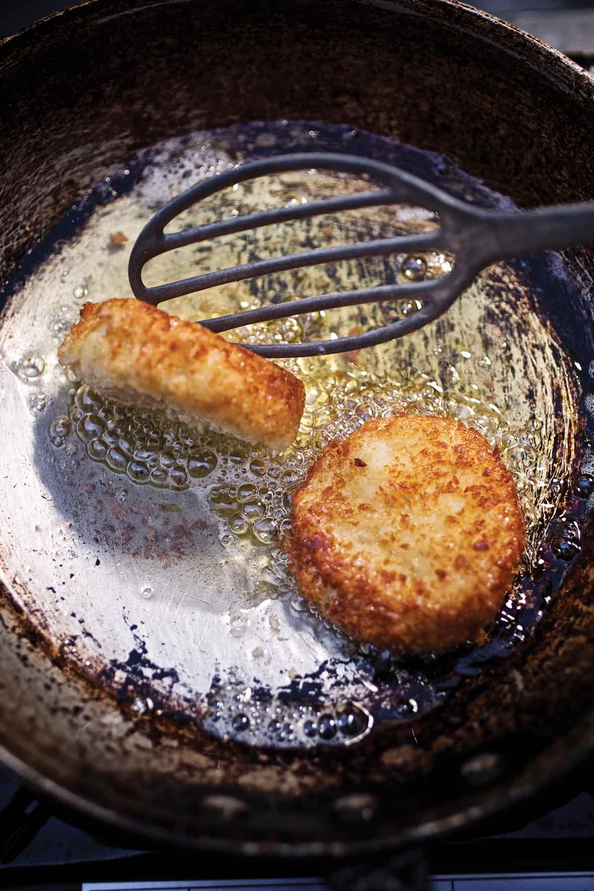 Old frying pan with two leftover mashed potato cakes being turned by a spatula