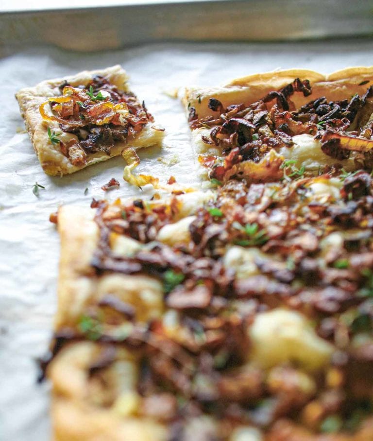 A sheet pan with an onion thyme tart on it, covered with cooked onions, thyme on a puff pastry crust