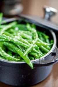 A cast-iron pot filled with pan-fried green beans tossed with garlic and butter