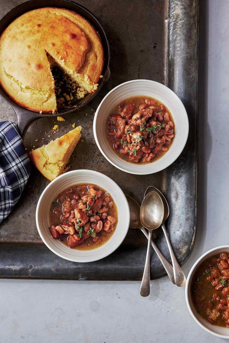 Three white bowls of pork and pinto beans chili on a metal tray with cornbread in a skillet