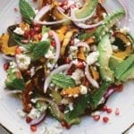 A plate of roasted delicata squash salad with red onion, feta cheese, avocado, and mint