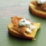 Two smoked trout crostini--toasted rustic bread with a flack of smoked trout and sour cream--on green wood table