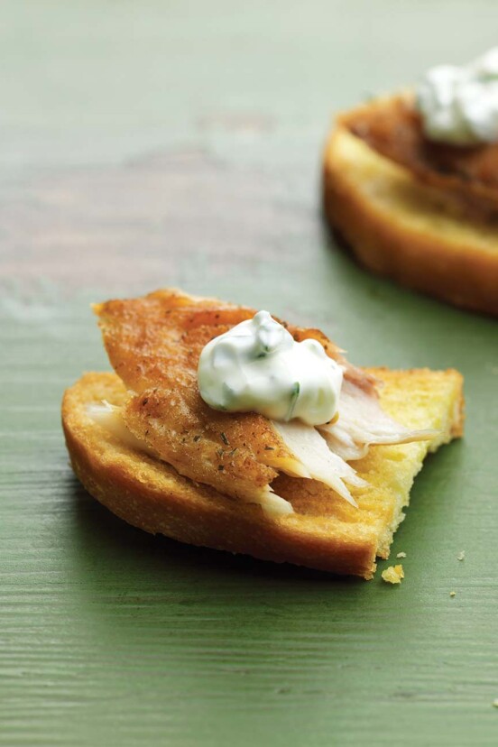 Two smoked trout crostini--toasted rustic bread with a flack of smoked trout and sour cream--on green wood table