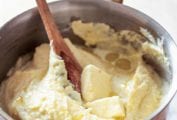 A pot of smooth mashed potatoes--made with plenty of butter, cream--with a wooden spoon and pat of butter on top