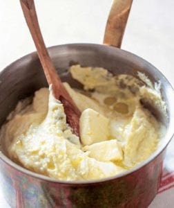 A pot of smooth mashed potatoes--made with plenty of butter, cream--with a wooden spoon and pat of butter on top