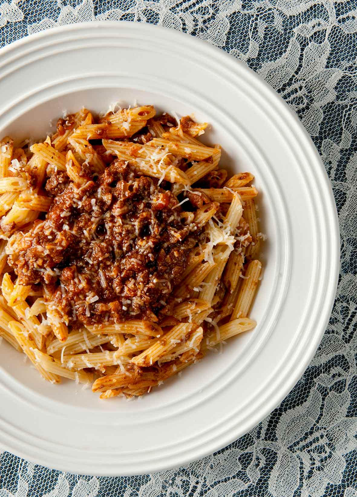 White bowl of venison Bolognese made with ground venison, carrots, onion, celery, mushrooms a top rigatoni.