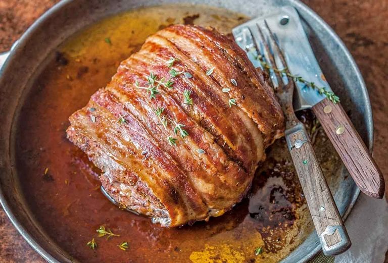 A plate with a bacon wrapped pork roast, rubbed with paprika, garlic, and cayenne, and topped with fresh thyme