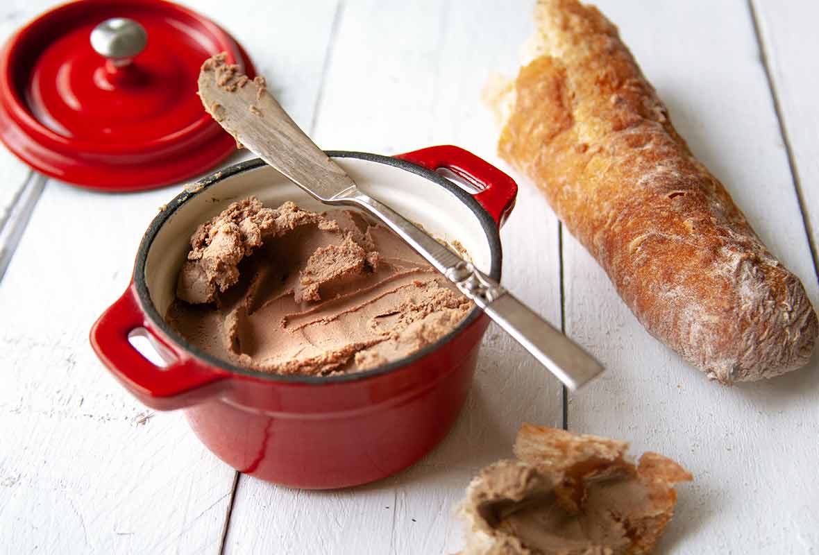 A small reck crock of easy chicken liver pate, nearby a baguette and and a hunk of bread smeared with pate