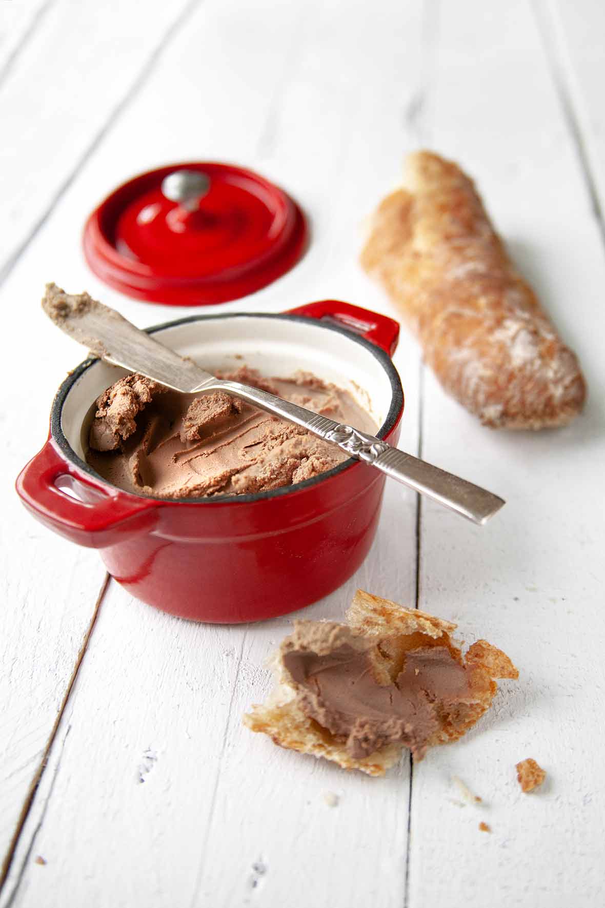A small reck crock of easy chicken liver pate, nearby a baguette and and a hunk of bread smeared with pate