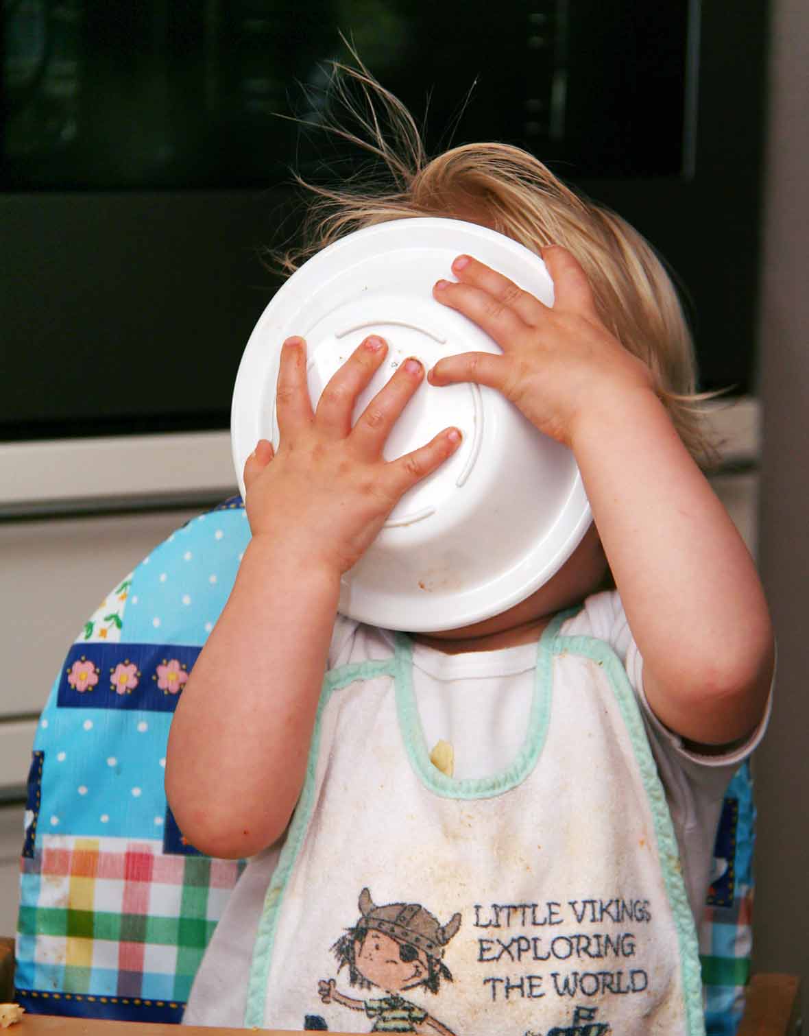 A kid in a high chair licking a bowl clean