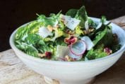 A bowl of a little gem salad--made up of little gem lettuce, radishes, shallots, walnuts, and walnut vinaigrette