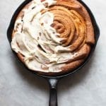 A giant skillet cinnamon roll in a black cast iron pan half cover with cream cheese icing.