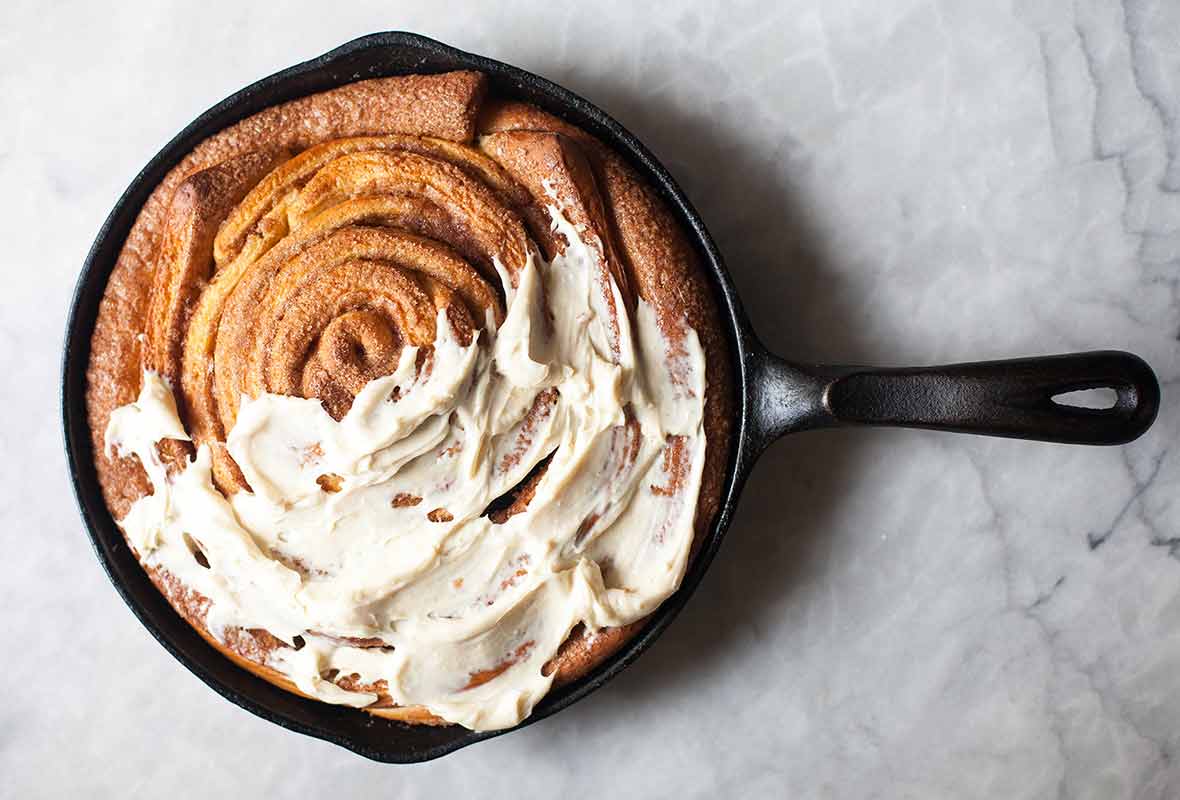 A giant skillet cinnamon roll in a black cast iron pan half cover with cream cheese icing