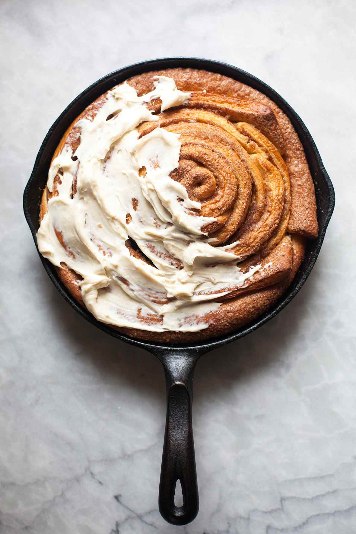 A giant skillet cinnamon roll in a black cast iron pan half cover with cream cheese icing