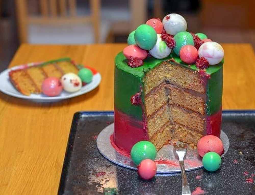 Three-layer vanilla paleo cake covered in red and green frosting and topped with candy globes