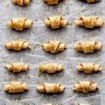 A baking sheet lined with parchment with 18 walnut rugelach cookies covered with brown sugar ready for the oven