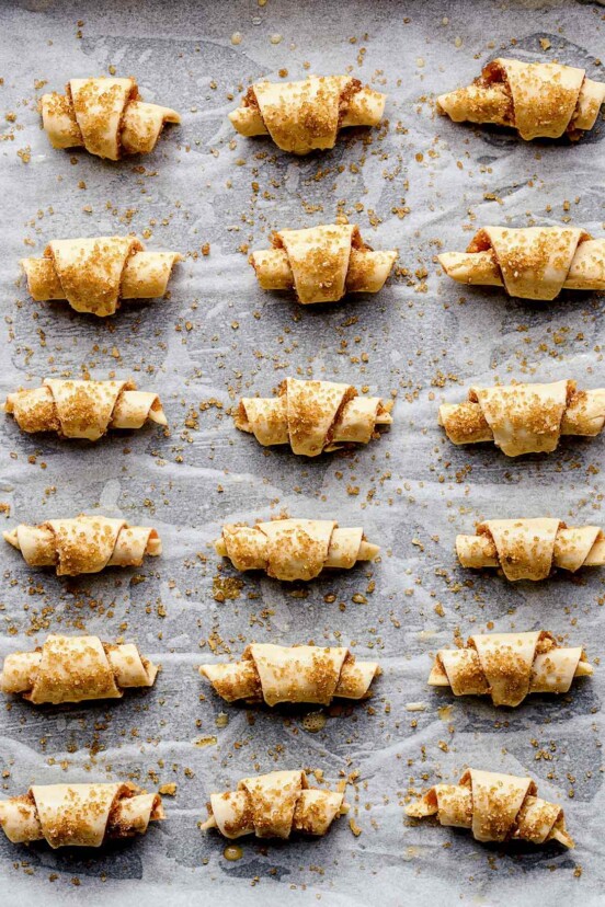 A baking sheet lined with parchment with 18 walnut rugelach cookies covered with brown sugar ready for the oven.