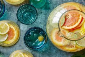 A pitcher and glasses of white sangria spritzer, filled with slices of lemons and oranges