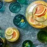 A pitcher and glasses of white sangria spritzer, filled with slices of lemons and oranges