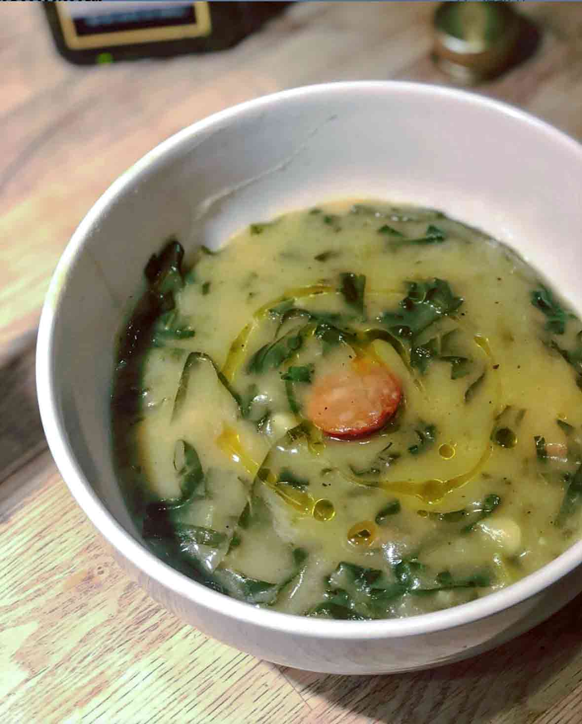A bowl of Portuguese soup called caldo verde--with puree potato, kale, and a slice of chouriço sausage