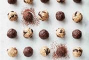 25 chocolate energy balls, made with dates, almond butter, almonds, and cacao powder, on white marble