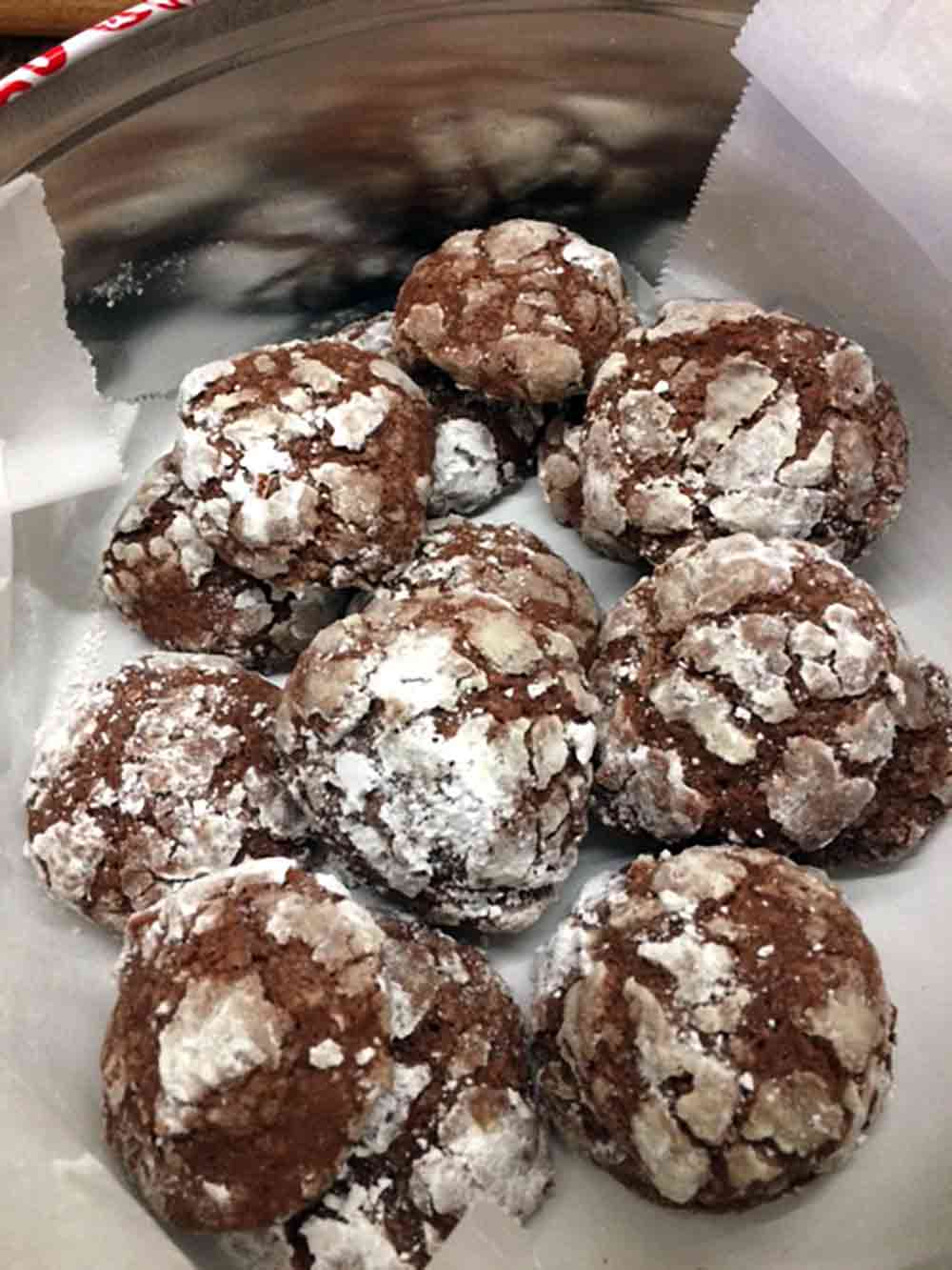A tin of chocolate-ginger crinkle cookies that are dusted with powdered sugar an covered in cracks