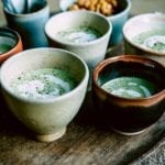 Four handmade bowls of green-speckled creamy broccoli soup with feta