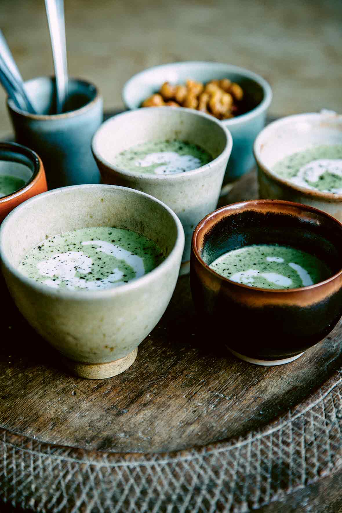 Four handmade bowls of green-speckled creamy broccoli soup with feta.