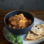 A bowl of devil's curry--chunks of chicken thighs, potatoes, and curry paste with naan bread on the side