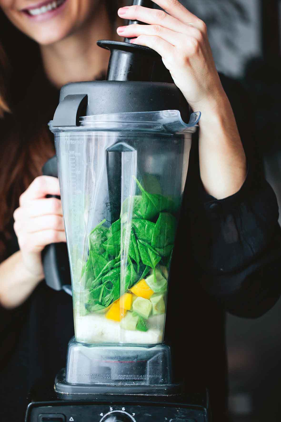 A woman with a Vitamix filled with spinach, mango, and milk