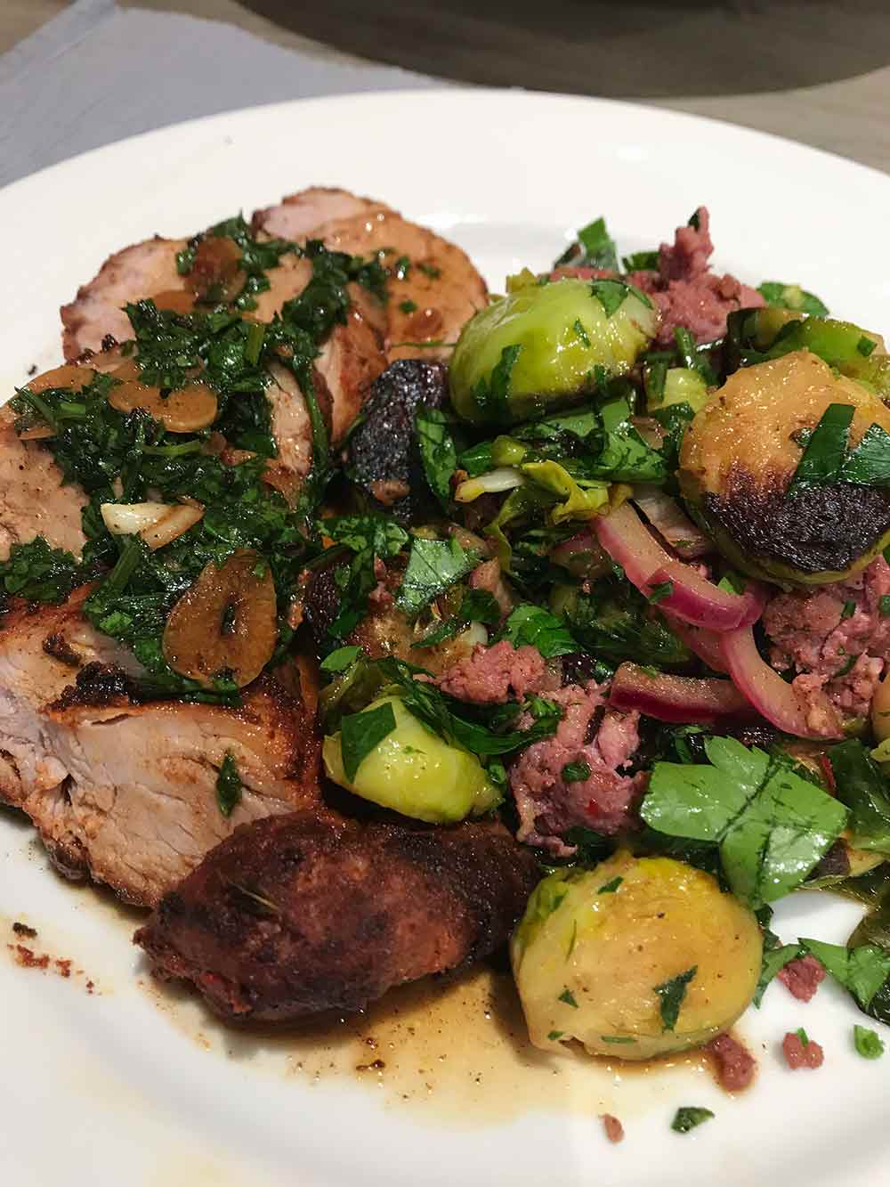 A plate with sliced roast pork tenderloin with paprika, potatoes, and Brussels sprouts