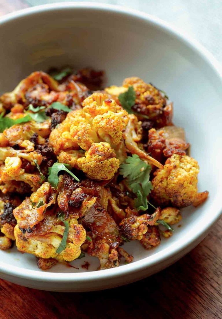 A bowl of roasted curried cauliflower mixed with onions and topped with cilantro.