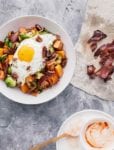 A bowl of roasted sweet potatoes and Brussels sprouts, onion, pecans, bacon and fried egg