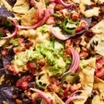 A close up of vegan nachos made with seitan, plus a sour lime cream, cashew, pickled red onions, avocado, jalapeño, and cilantro