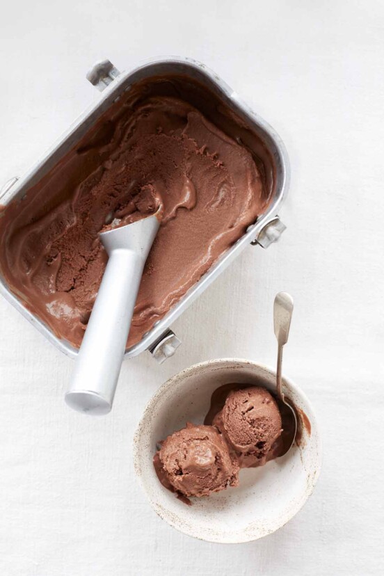 A tub of vegan peanut butter pice cream with a bowl of two scoops on the site