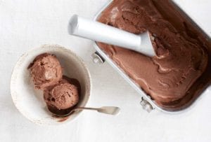 A tub of vegan peanut butter pice cream with a bowl of two scoops on the site