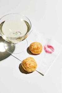 Two best gougeres on a cocktail napkin with a lipstick print on it and a glass of Champagne