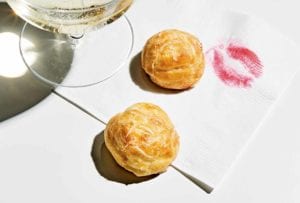 Two best gougeres on a cocktail napkin with a lipstick print on it and a glass of Champagne