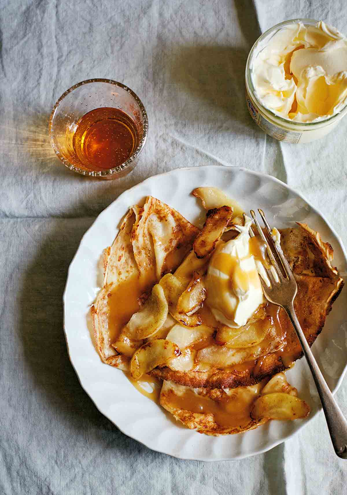 A white plate filled with crêpes dentelles with sautéed apples and caramel sauce