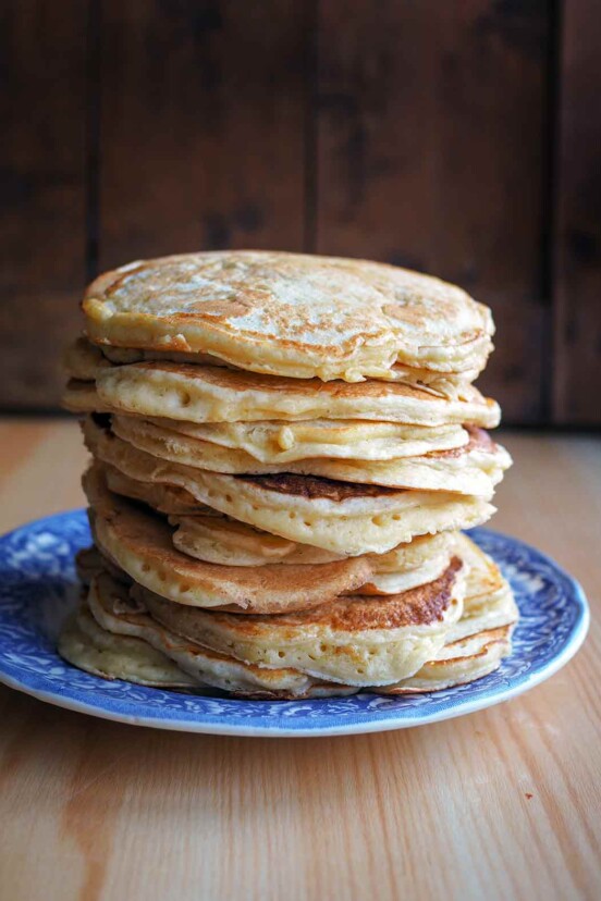 A blue plate piled with a stack of griddle cakes.