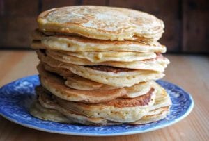 A blue plate piled with a stack of griddle cakes