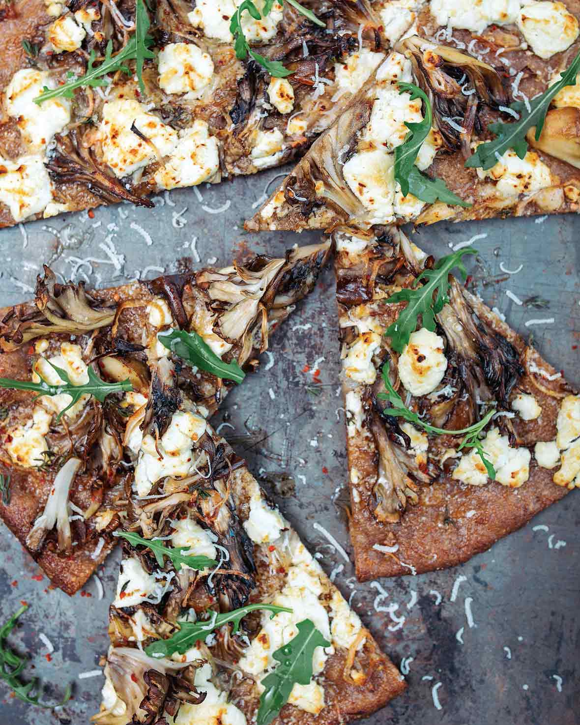 A mushroom and goat cheese pizza topped with dandelion leaves cut into six slices